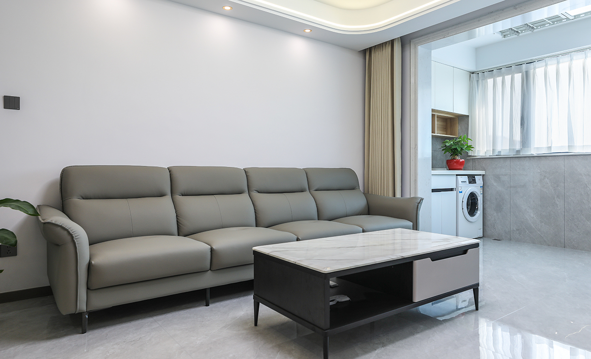 沙發(fā)背景刷米灰色涂料，白色的沙簾，沙發(fā)背景留白設(shè)計(jì)，色調(diào)上墻面涂料和窗簾用淺色，沙發(fā)用深色，深淺搭配的錯(cuò)落有致，既溫馨又簡(jiǎn)潔。
