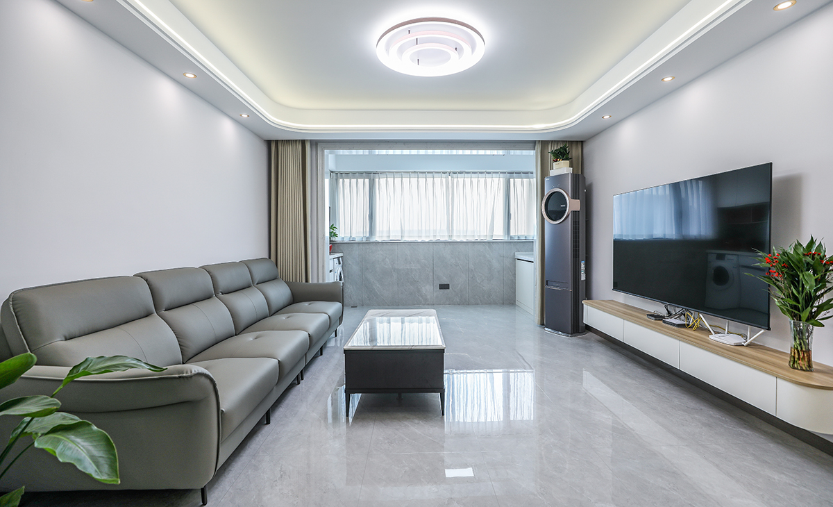 客廳開(kāi)間很大，電視墻做的是調(diào)色乳膠漆和懸空電視柜相互配合，明暗有神，深灰色皮質(zhì)沙發(fā)立刻檔次提高很多，把南陽(yáng)臺(tái)移門拆除后，客廳空間也很寬闊。吊頂造型上采用圓弧性雙眼皮吊頂+線性燈點(diǎn)綴。地面采用淺灰色地磚。造型和色調(diào)上無(wú)不給人以簡(jiǎn)潔、大氣、時(shí)尚的感覺(jué)。