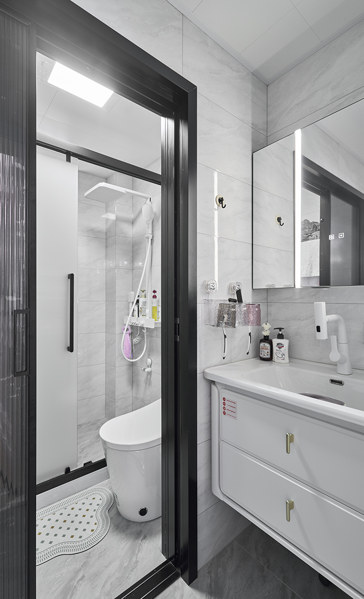 衛生間采用干濕分離的布置，淺灰色墻磚配白色浴室柜和黑色邊框長虹玻璃移門，顏色明暗有序，從深到淺，色調很豐富，掛墻臺盆柜，墻排水設計，下方又設計一個地漏，顏色協調統一，主人很滿意。  