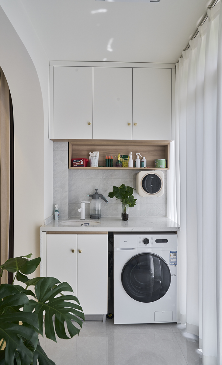 該套房子陽臺的空間利用的很完美，定制洗衣機柜，儲物空間很大，有一個小水池也能洗洗小東西，上面做一個吊柜，留一開放格放經常用的物品，使用起來很方便，把空間襯托的完美無霞。