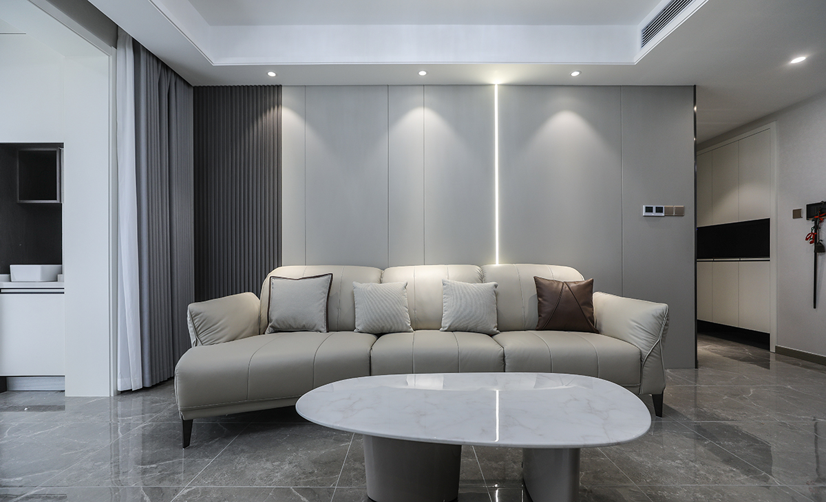 沙發(fā)背景刷米灰色涂料，白色的沙簾，沙發(fā)背景留白設(shè)計(jì)，色調(diào)上墻面涂料和窗簾用淺色，沙發(fā)用深色，深淺搭配的錯(cuò)落有致，既溫馨又簡(jiǎn)潔。