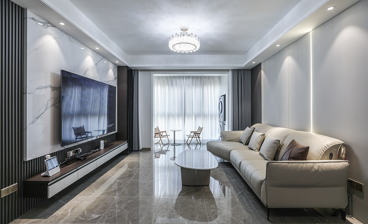 客廳開(kāi)間很大，電視墻做兩片巖板，兩塊木飾面，淺的巖板和原木色木飾面相互配合，明暗有神，深灰色皮質(zhì)沙發(fā)立刻檔次提高很多，放一組貴妃沙發(fā)，客廳空間也很寬闊。吊頂造型上采用雙眼皮吊頂。地面采用淺灰色地磚。造型和色調(diào)上無(wú)不給人以簡(jiǎn)潔、大氣、時(shí)尚的感覺(jué)。