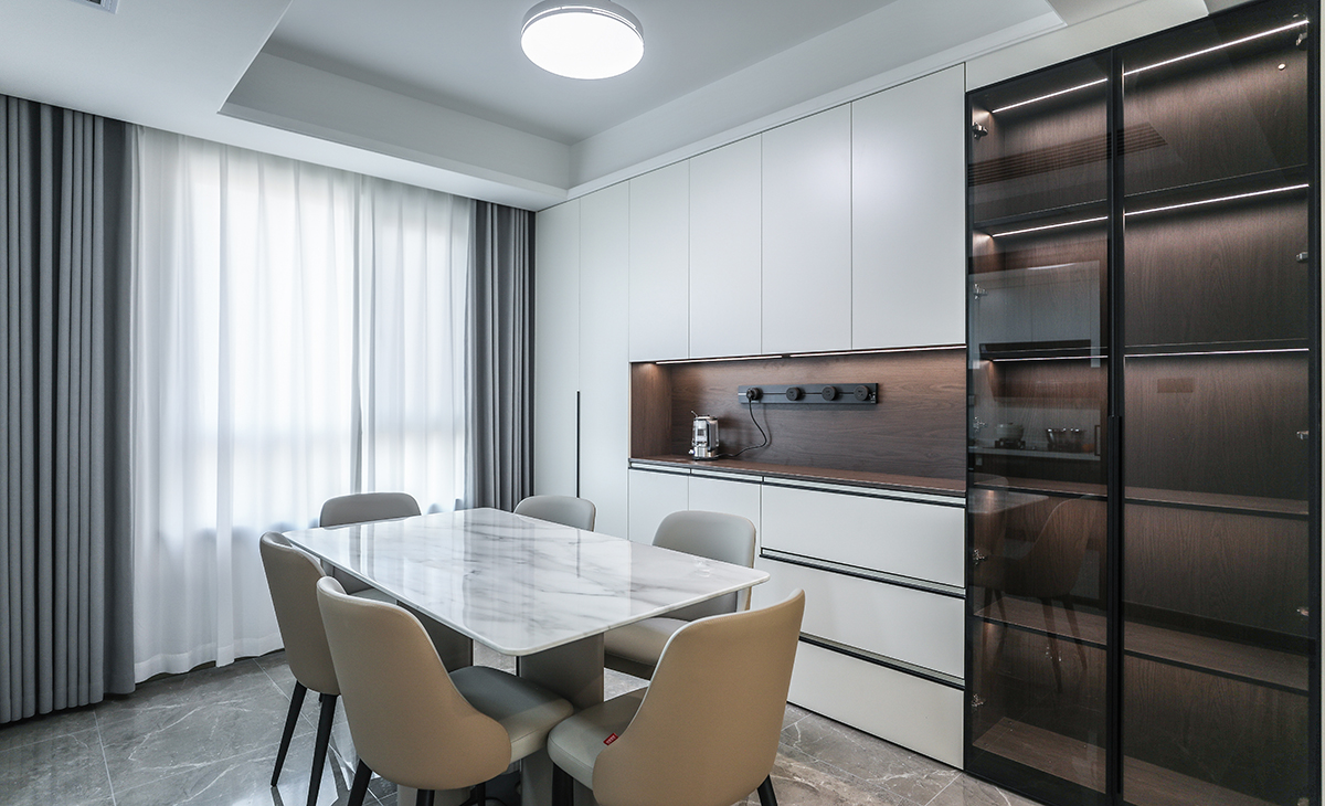 餐廳空間比較方正寬敞，又有一個(gè)大飄窗，靠墻做一排裝飾柜，既實(shí)用、又有裝飾功能，原木色框架，極窄邊框玻璃門(mén)和白色木門(mén)板相呼應(yīng)，巖板餐桌把用餐氛圍調(diào)和的很溫暖，淺灰色地磚很干凈，色彩和造型上都簡(jiǎn)潔大氣。