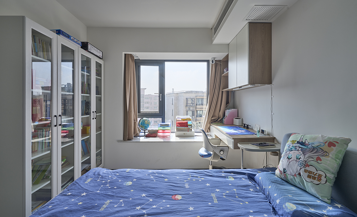 兒子房也有大飄窗，利用飄窗做一個懸挑寫字臺，上面吊柜，寫字臺對面又有一排書柜，有效收納了兒子的書籍。
