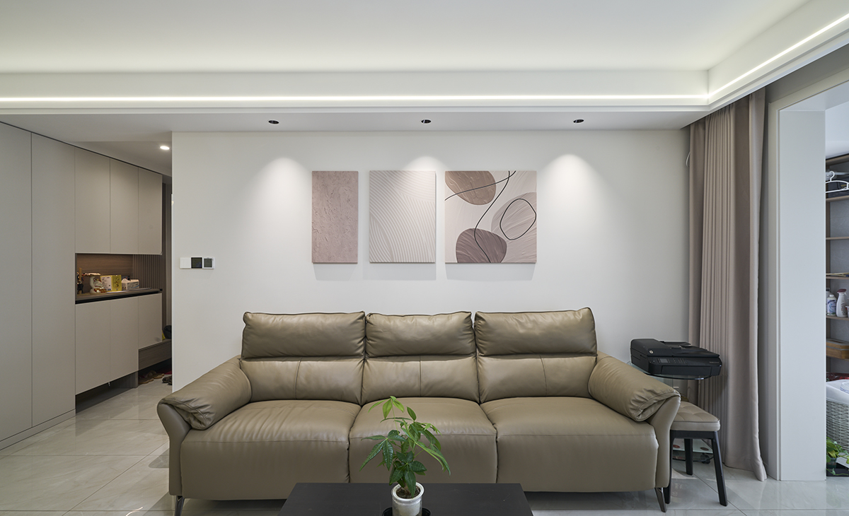 沙發背景墻上3副大小不一的掛畫，盡顯活潑生動，頂上三個射燈點綴的恰到好處，讓客廳整個空間感覺簡潔清爽。