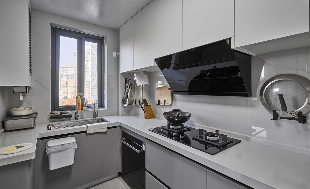 該套房子廚房空間很大，做成U字型櫥柜，洗碗機采用嵌入式，煤氣灶下方配洗碗機，上柜采用白色柜門，臺面白色，下柜采用淺灰色方便打理，墻地磚的顏色和櫥柜顏色搭配地很自然，客戶不斷地夸贊設計師對色彩的精準把握。