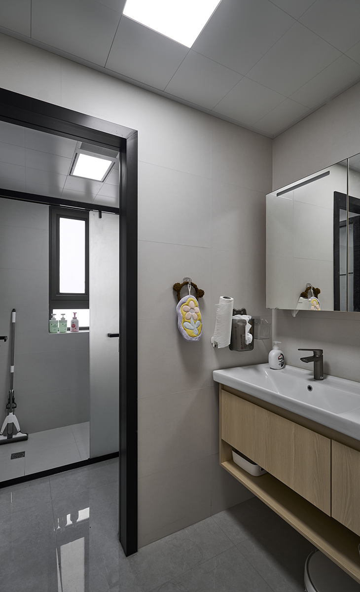 衛生間采用干濕分離的布置，淺灰色墻磚配原木色浴室柜和黑色邊框長虹玻璃開門，顏色明暗有序，從深到淺，色調很豐富，掛墻臺盆柜，墻排水設計，下方又設計一個地漏，顏色協調統一，主人很滿意。