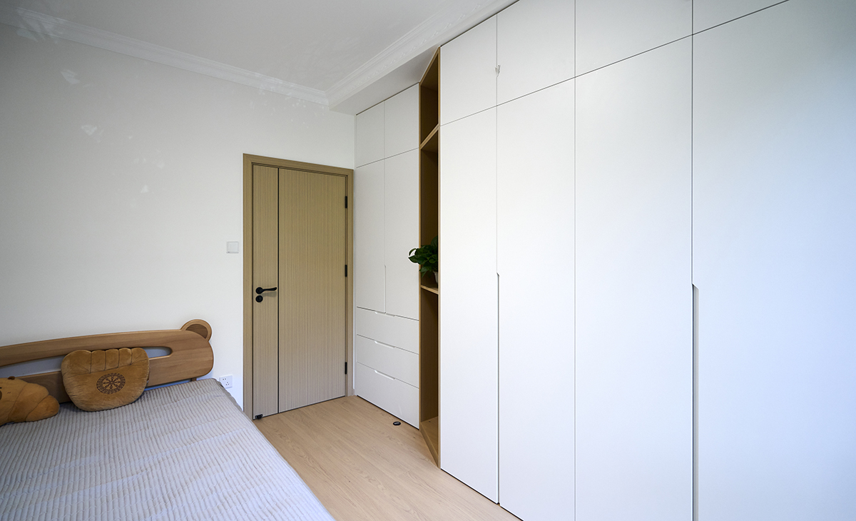 次臥做滿墻儲物柜，厚度上深淺有致，靈活生動，不呆板，原木色框架+白色平板柜門，既簡潔又方便清理。