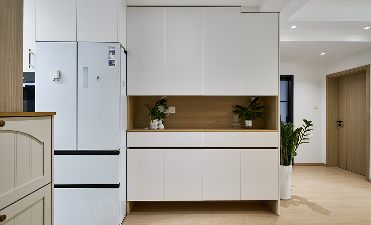 進門玄關柜很大，中間漏空放綠植、下方漏空放鞋，旁邊就是嵌入式冰箱，可以充分利用儲物空間，淺灰色套裝門和踢腳板，空間很寬敞。