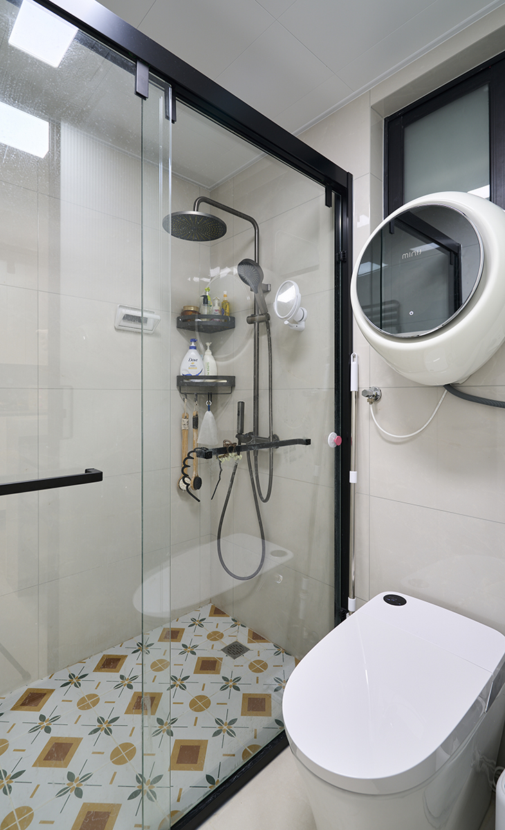 衛(wèi)生間采用干濕分離的布置，淺灰色墻磚配深灰色色浴室柜和黑色邊框長(zhǎng)虹玻璃移門(mén)，顏色明暗有序，從深到淺，色調(diào)很豐富，掛墻臺(tái)盆柜，墻排水設(shè)計(jì)，下方又設(shè)計(jì)一個(gè)掃地機(jī)器人，顏色協(xié)調(diào)統(tǒng)一，主人很滿(mǎn)意。  