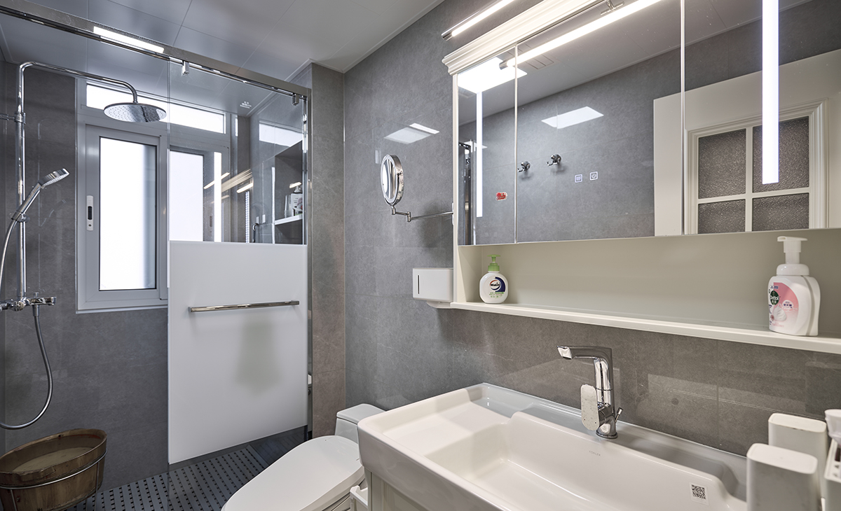 衛生間采用干濕分離的布置，淺灰色墻磚配白色浴室柜和黑色邊框長虹玻璃移門，顏色明暗有序，從深到淺，色調很豐富，掛墻臺盆柜，墻排水設計，下方又設計一個地漏，顏色協調統一。 