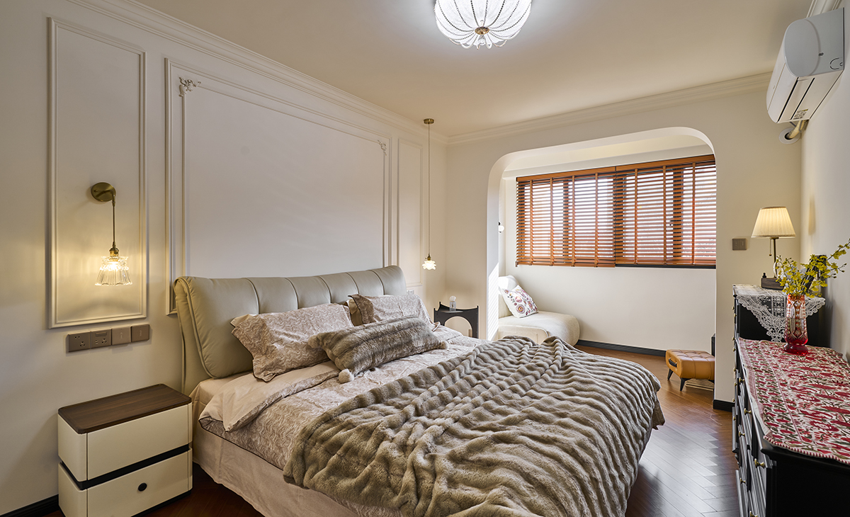 主臥床尾拱形門洞連接白色單人沙發與木質邊幾，木質百葉窗過濾自然光，營造半私密休憩區。