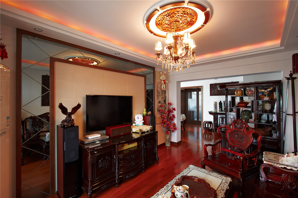 由于客廳不是很寬，且客戶配備的是色系較深的中式家具，使得原本狹小的空間更加擁擠，于是在背景墻采用了米色皮紋磚與灰鏡相結合，灰鏡使得狹窄的空間變得寬。米色的皮紋磚更加襯托了家具的質感，木線條的色系與家具相得易章，協調統一。
