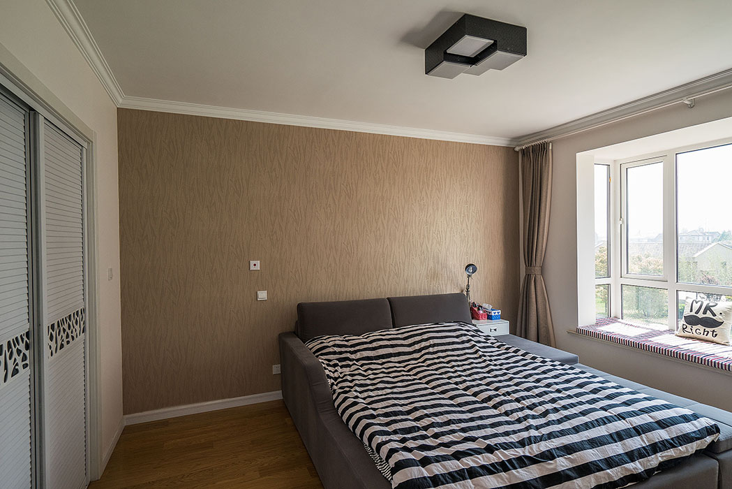 對于臥室來說，黑白兩色過于簡單，所以設(shè)計師加入了色澤多樣的軟裝墻紙，盡量使這里體現(xiàn)出溫馨，背景墻咖啡色墻紙與白色的融合，卻富有現(xiàn)代感。