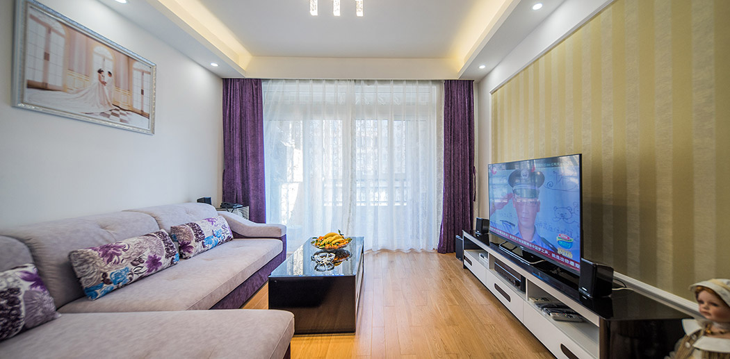 客廳采用簡約式的長條吊頂，加上暗藏燈帶的設計，使得室內整體光線更加的柔和、溫馨，長形吊頂使得空間拉伸，視覺空間上更加強烈，簡單而時尚的吊燈加上淺色的地板，使得客廳這個主要活動區更加的清新脫俗。
