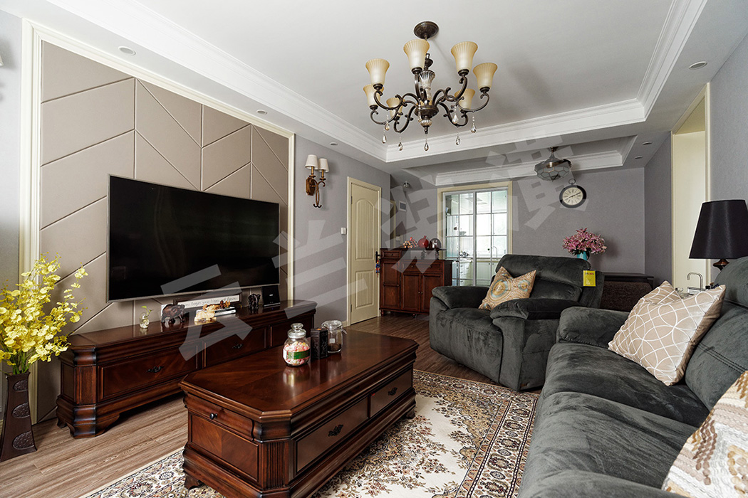 客廳的整體色調(diào)和質(zhì)感偏濃重，作為點睛之筆的電視背景墻，線條明朗的灰色硬包在乳白色木線條的襯托下與沉穩(wěn)大氣的深色家具相呼應(yīng)，家具又與藍(lán)灰色墻面形成反差，凸顯了客廳的立體感和層次感。
