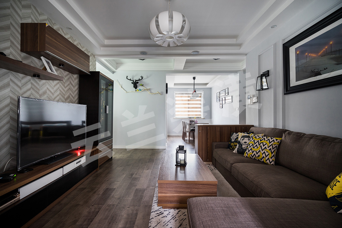  現代人們越來越喜歡簡單化的家具，它舒適更便于打掃，所以客廳的家具雖保持著美式的沉穩顏色，但是沒有了繁瑣的花紋和配飾。那更多美式的元素就是藏在與吊頂和立面簡單的畫框線條。他的吊頂更多的是層層疊加，讓整個立面看上去更立體。再配上客戶花心思淘的配飾和掛畫，讓整個空間一下子生動了起來。客廳的整個立面設計都已經簡單化，已有了沙發背景的線條框，所以電視背景只采用了簡單的墻紙來修飾在配上組合柜來豐富整個格局。最后加上顏色亮麗的掛畫和抱枕讓整體空間都生機勃勃了起來。
