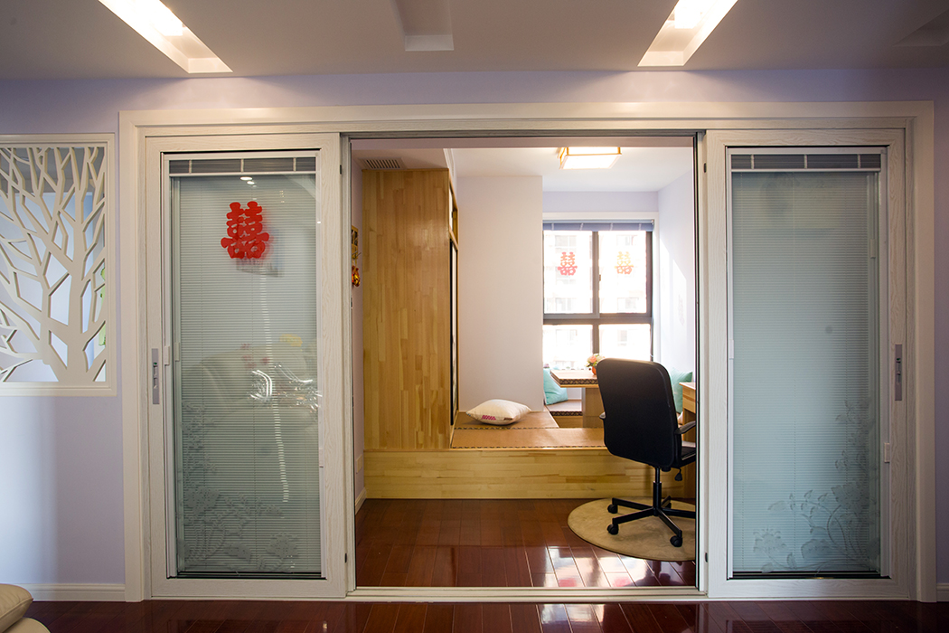 因為過道比較狹長，所以在設計中將臥室的墻面打通，和客廳融為一體，做成榻榻米多功能區域，可以和朋友聊天，可以當書房，家人來了也可以小住。四扇玻璃隔斷移門，更好的化解了過道的單調性。
