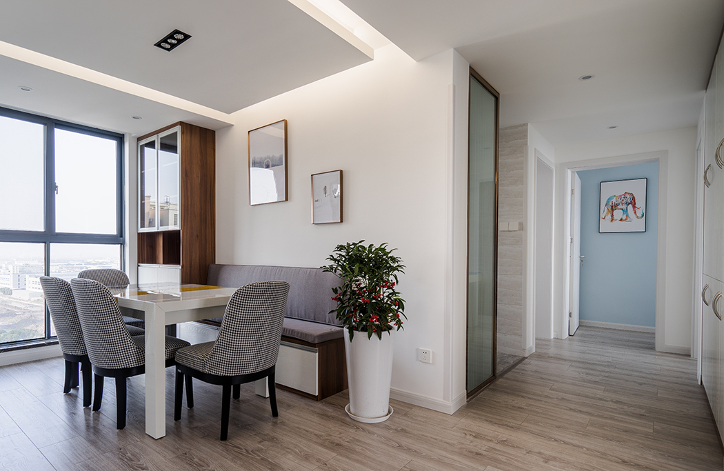 餐區通過大體塊的墻頂體留白和溫潤細膩的地板色形成對比，與此呼應的是同色調的餐桌椅，而綠色、玫瑰金的邊框色則延續了主空間的點綴色，淺紫色的抽象裝飾畫與餐桌旁邊的綠植、夾絲玻璃的金屬色作為一個整體貫穿于整個空間，點燃了熱情。冷暖色調的跳躍搭配豐富整體設計的層次感，而華麗精美的射燈造型，傾瀉出迷醉溫柔的燈光讓空間每一件家具飾品都成為無可挑剔，不可或缺的藝術品。
