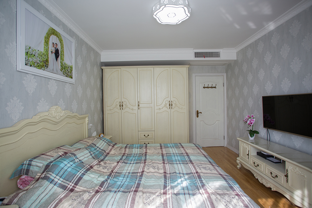 主臥室墻面貼的是淺灰色無紡布，搭配象牙白的整體家具，主臥朝南，陽光照進臥室顯得格外溫馨。
