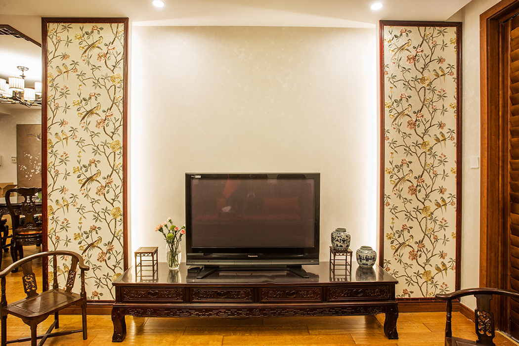 客廳吊頂與餐廳吊頂相統一，但只有這些也是不夠的，將中式元素的花鳥壁紙設計在電視背景墻之中，看起來就像兩扇中式屏風，加入木線條更顯沉穩內斂。
