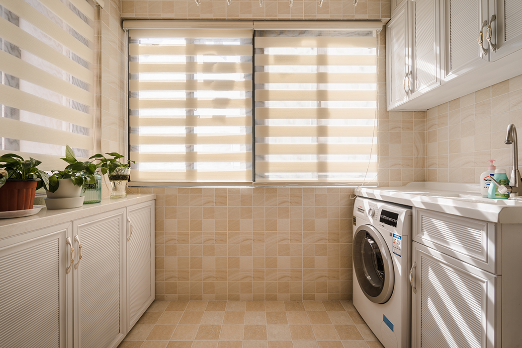 花格子墻磚，半通透式的窗簾，成品洗衣搭檔，使整體陽(yáng)臺(tái)美觀與實(shí)用完美結(jié)合，矮柜上的綠色盆景，為整個(gè)空間增添了一份活力。
