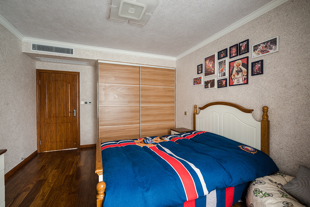 次臥還是征求了業主兒子的喜好，以現代偏英倫風格來裝飾，墻頂面都改用墻紙來打底和臥室客廳風格完全不同，但局部的深色家具很好的呼應了門套和窗套，讓區域和區域也融入一體。
