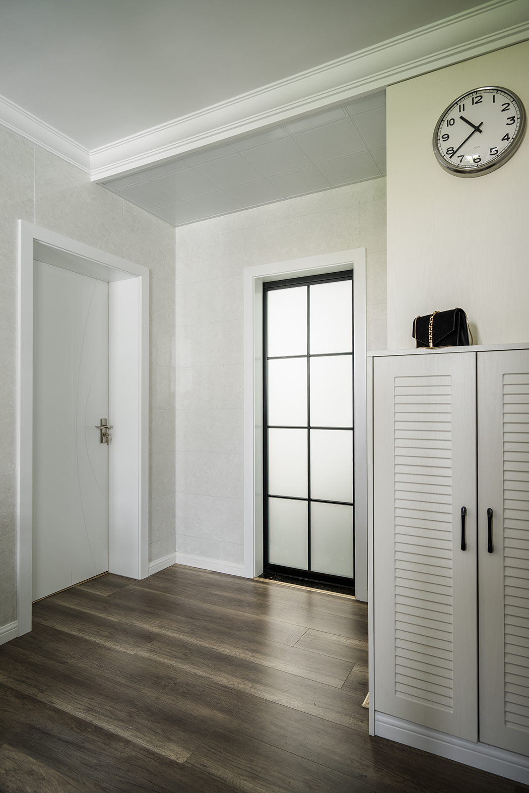 客餐廳的背景采用了白色文化石，作為餐廳的背景材料增加了整體的檔次，玄關(guān)鞋柜上的小鐘更突顯出業(yè)主是個注重時間效率的人。整體的室內(nèi)設(shè)計，以現(xiàn)代簡約為主，配以極簡現(xiàn)代又時尚的風格點綴。百葉門的鞋柜對整體風格也起到提亮的效果。