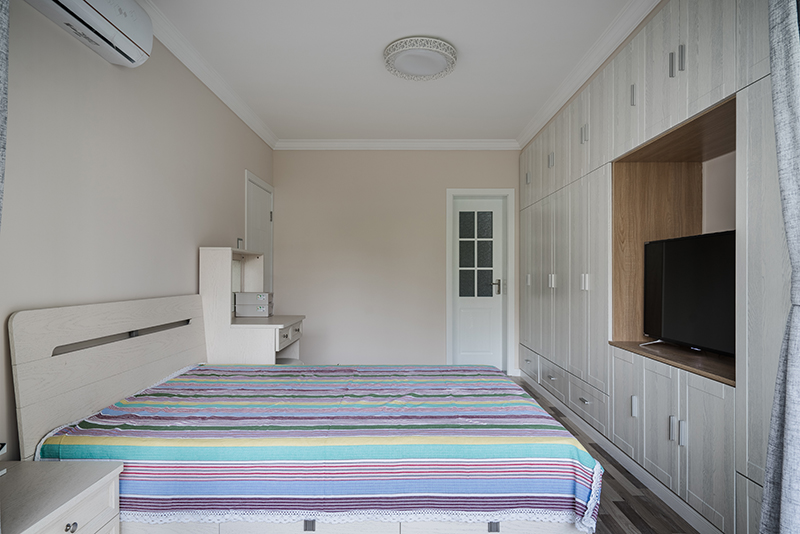 主臥的格局就是三面墻都有門，所以為了考慮足夠的儲物空間還有美觀，還按照整體的色調(diào)現(xiàn)場制作了這個儲物電視一體柜，墻面淡淡的白駱駝色又給人很溫馨的舒適感。
