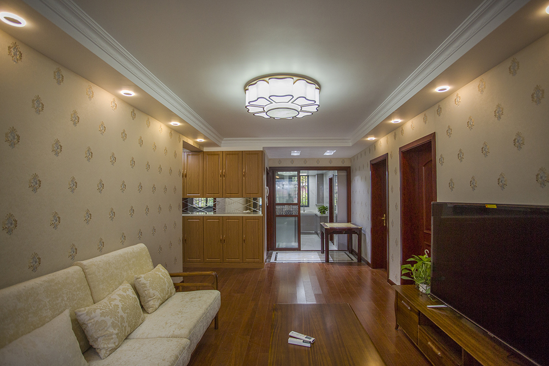 客廳作為一個家的代表，暖色花紋的壁紙，打造出溫馨莊重的背景，胡桃木色的家具，本應給厚重的空間更增加一些厚重感，卻采用了形式簡潔的沙發，給厚重的空間增加了一些空靈，空間整體融合了冷暖，厚重與空靈.
