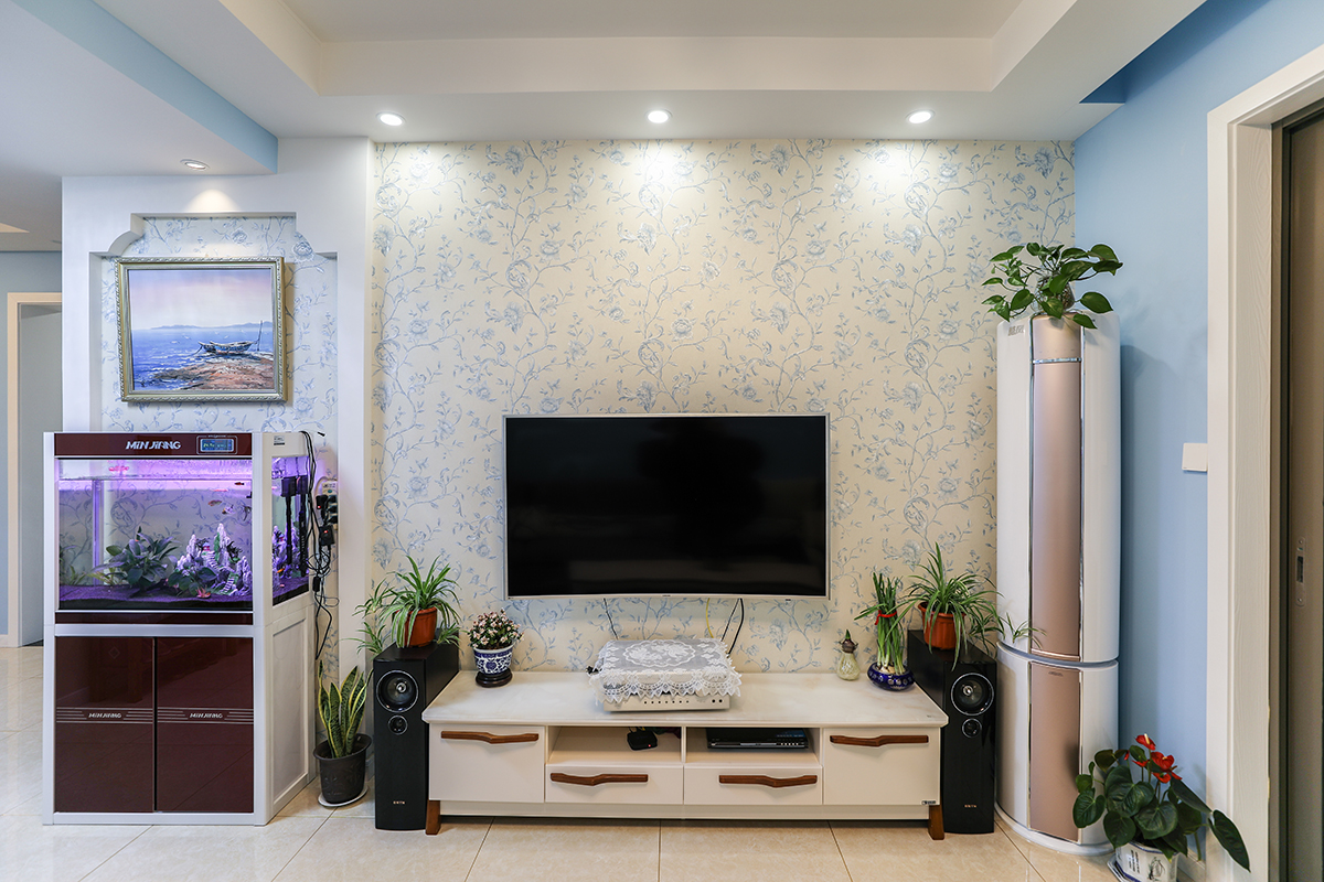 電視背景墻是以白色為底色加藍(lán)色小花的墻紙，白色實(shí)木低柜突出其線條，與整體風(fēng)格相融合，旁邊的魚(yú)缸為家增添了幾分生氣。 

