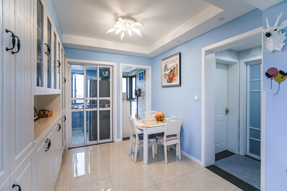 餐廳地面使用淡黃玻化磚，大氣明亮。淡藍(lán)色墻面，加上白色的模壓門(mén)板酒柜，白色餐桌，還有白色門(mén)套，祥和舒適。
