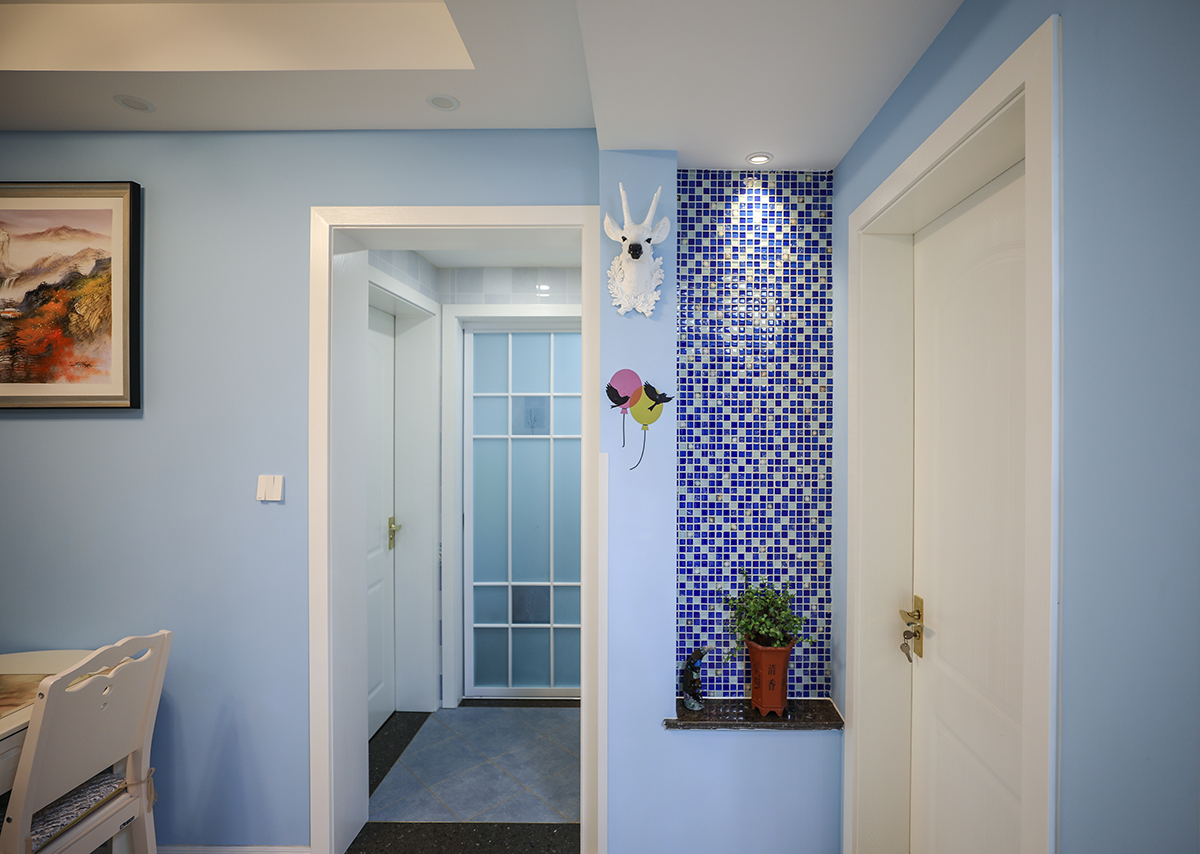 玄關(guān)處延續(xù)并深化了藍(lán)色調(diào)，采用藍(lán)白相間的馬賽克磚作為背景，再來(lái)一盆綠植點(diǎn)綴，更加富有生氣。