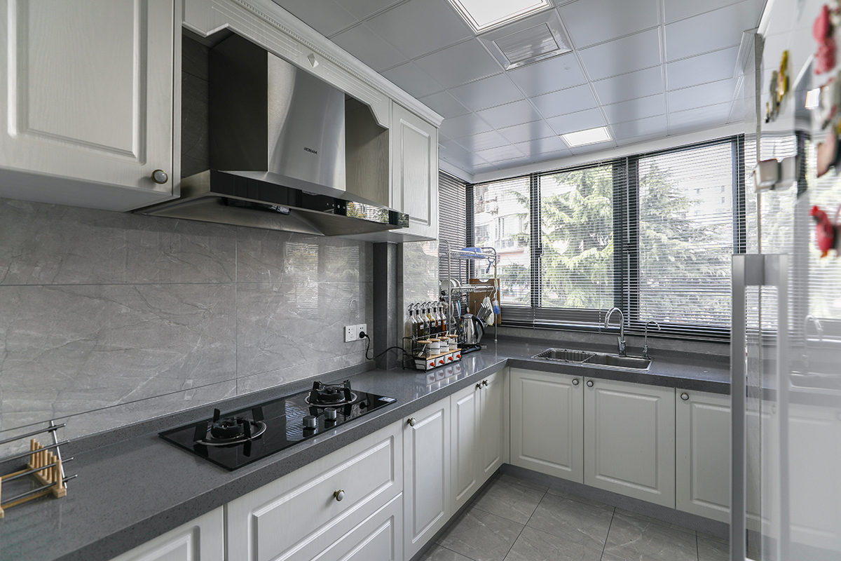 原本狹小的廚房和工作陽臺打通之后，變得寬敞明亮，整體使用灰色的玻化磚，大氣時尚，又和深灰色臺面相呼應，同時和白色模壓門板的櫥柜形成對比。
