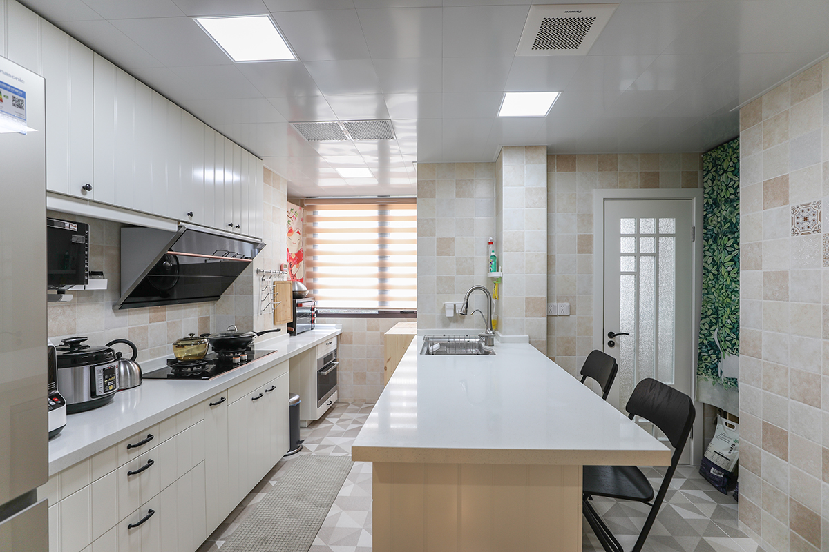 業(yè)主選用開放式的廚房，打破了原始戶型的結構，改變了格局，重新進行設計。白色的高光門板色，配上黑色的拉手，帶著白色門板上的簡單線條，整個空間既大氣又敞亮。廚房間的中島，既能當做操縱臺面，又能切菜、配菜，當餐桌用。中間的水槽，是典型開放式廚房，中島櫥柜的設計。深受廣大業(yè)主的喜歡。小方格的墻磚，配上三角的磚，立體感特別強。把原始廚房間的墻面，往衛(wèi)生間的空間里推進去幾公分，整個開放式的廚房間很寬敞。熱水器上用了一個招財貓的簾布，米黃色的墻面，配上紅色喜氣的簾布，整個空間更有靈動性。
