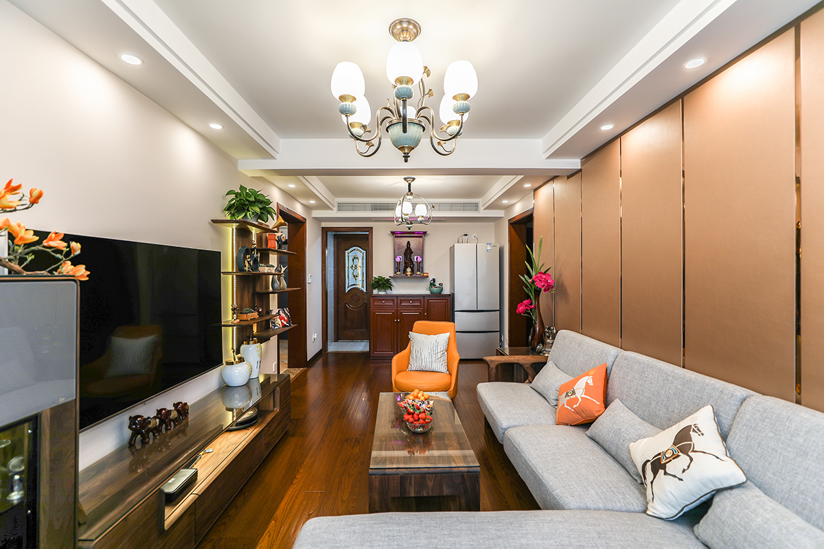 客廳整體風格采用硬包，組合柜，金屬條，香檳色硬包搭配金屬條，曾加了整體的時尚感 。電視組合柜簡約不簡單，深色木質給整體增加一絲沉穩大氣，灰色沙發搭配橙色單椅，舒適加上色彩的跳躍，讓整體不沉悶。
