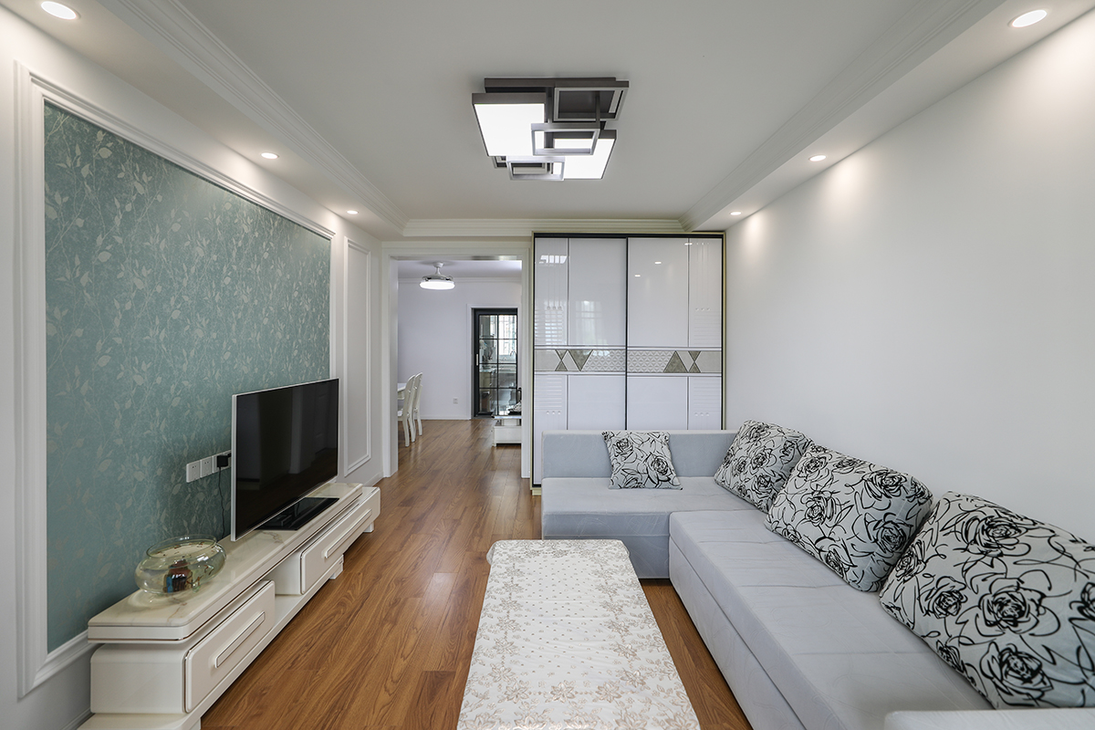 該套房客廳是由原來的臥室改造而成，光線不太明亮，所以整體以白色為主，配上灰色的沙發，現代時尚的吸頂燈，使空間干凈清爽、豐富多彩，不單一呆板。
