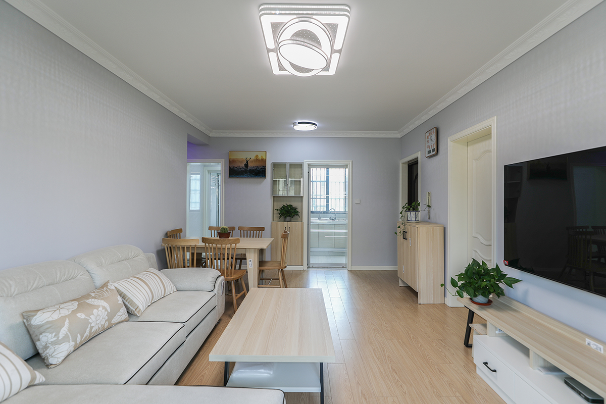 客廳整體墻面選用淺灰色，頂面走歐式石膏線，與簡歐踢腳線做上下呼應(yīng)，簡單而不單調(diào)。軟裝方面，灰藍(lán)色的窗簾與墻面裝飾畫相近色的色彩運(yùn)用，凸顯層次感。用白色的布藝沙發(fā)與灰色墻面交相呼應(yīng)溫馨而不突兀。暖色的地板及原木的桌椅中和掉整個空間的冷意。
