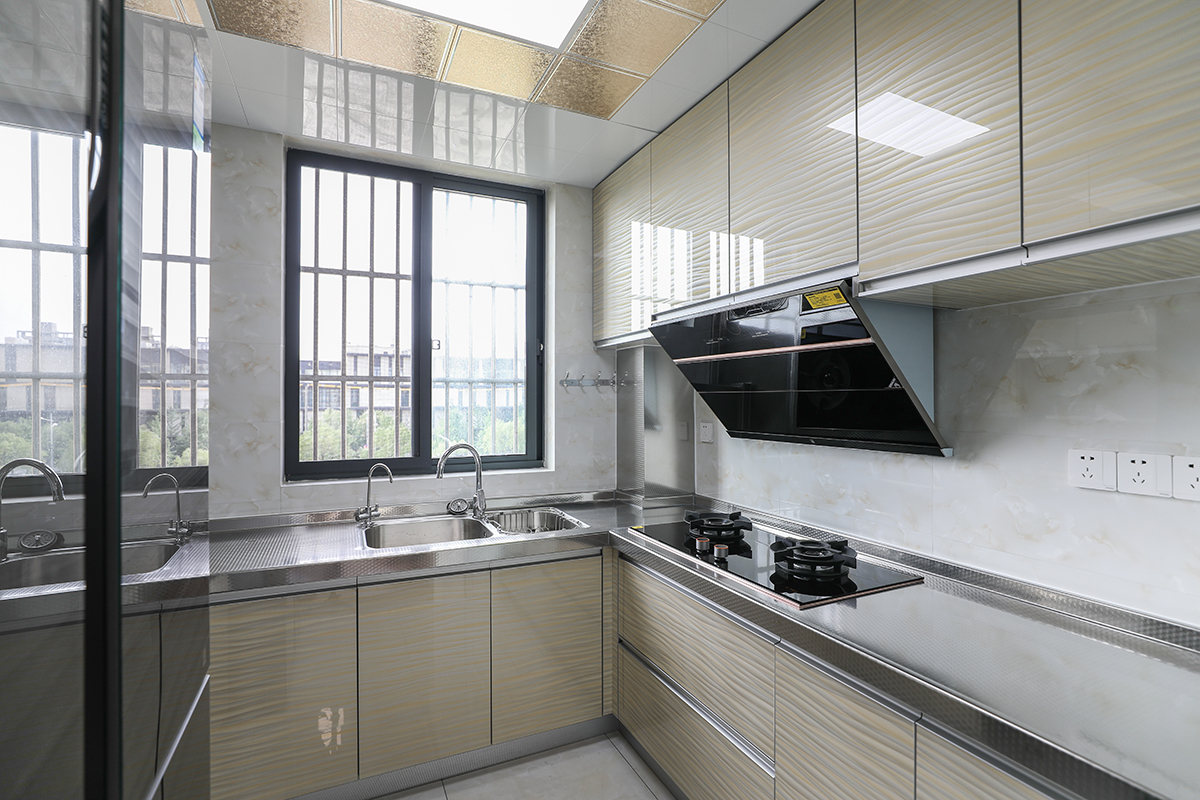 廚房臺面選用304不銹鋼，與不銹鋼水槽焊接一體，方便清潔打理。整個空間顯得明亮。廚房櫥柜門板選用波浪紋亞克力門板。暖色調(diào)的運(yùn)用中和了臺面的冰冷。
