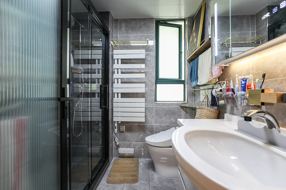 衛生間灰色瓷磚，白色的潔具搭配黑色邊框的淋浴房永遠是那么的經典，電加熱毛巾架的使用也是非常的貼心，在寒冷的冬天給人一絲絲的暖意。