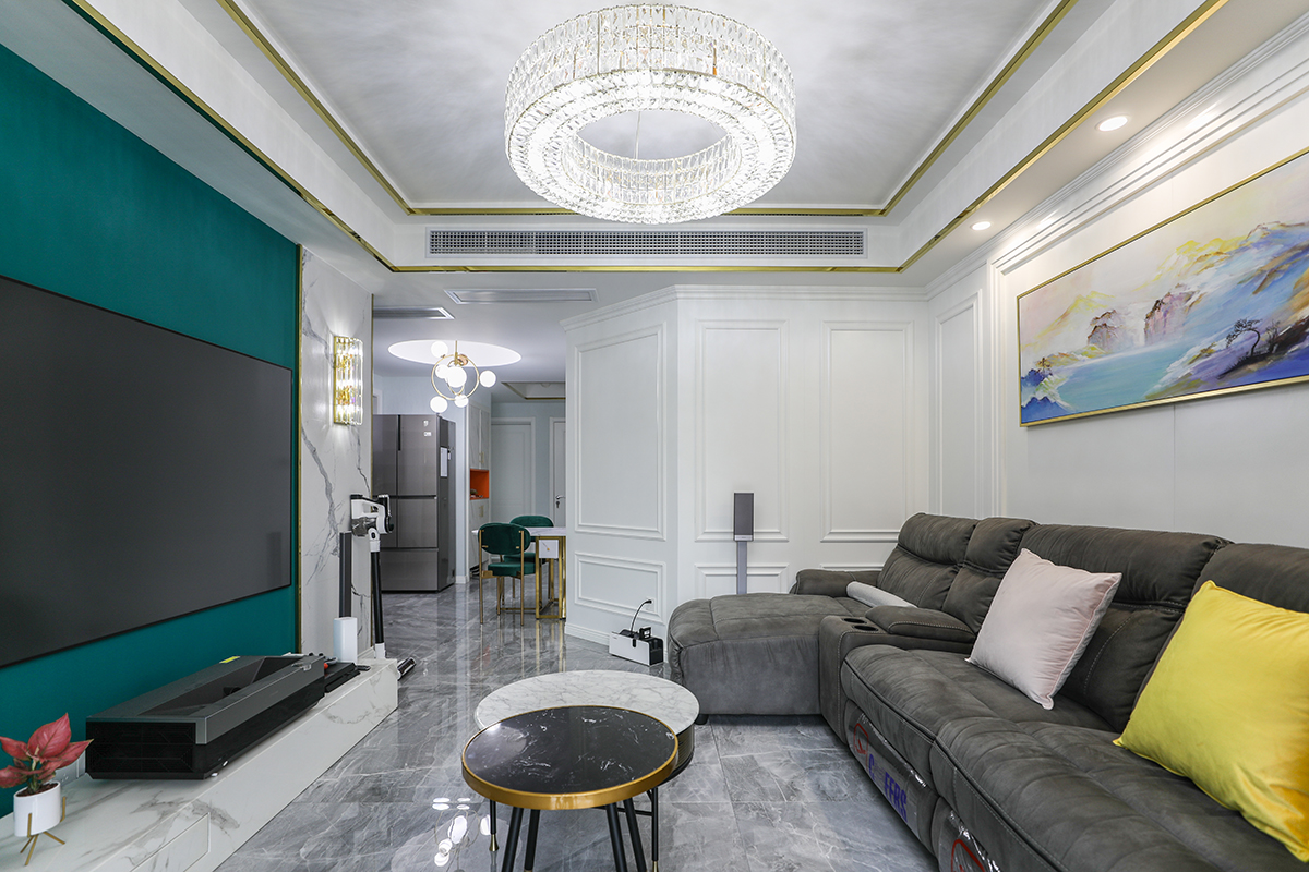 客廳整體風格采用木，鏡，沙風格，是當下比較時尚也是板式的處理方式，在顏色上做了調色，配上精致的玻璃燈和線簾的裝飾，把板式的硬線條做了軟性富有穩重。黑色的皮沙發，配上灰色的地磚，有層次感的護墻板，更彰顯出了整體的效果。電視背景墻，采用輕奢通用的爵士白上墻，再配上不銹鋼線條，中間是墨綠色的墻紙，細節附金色系裝飾點綴，時尚大氣。客廳的茶幾和電視背景墻的大理石相呼應，茶幾側面的鏡色玻璃和茶幾的金屬線條。窗簾上的檸檬黃，和沙發上的檸檬黃抱枕相呼應。客廳頂上的水晶燈，配上輕奢的金屬鋼線條搭在一起，使家里輕奢的效果更沉穩。紅色的綠植在灰、綠、金屬鋼線條之前，作為點綴。
