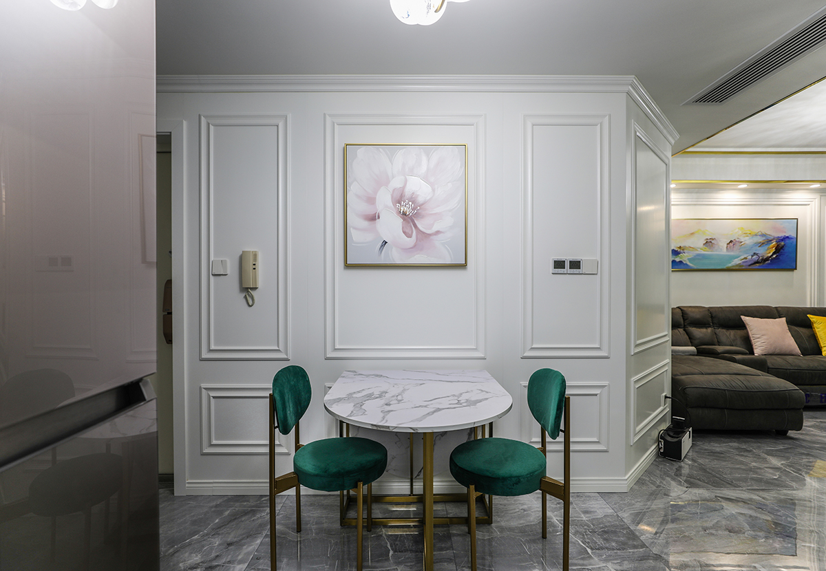 餐桌的那面墻，配上白色的護墻板，中間掛了一副粉色的掛畫，配上有金屬線條的邊框，跟客廳的效果相呼應，墨綠色的桌椅，大理石的桌面，帶有金屬線條的桌角，使得客廳和餐廳更諧、穩重、時尚、大氣。
