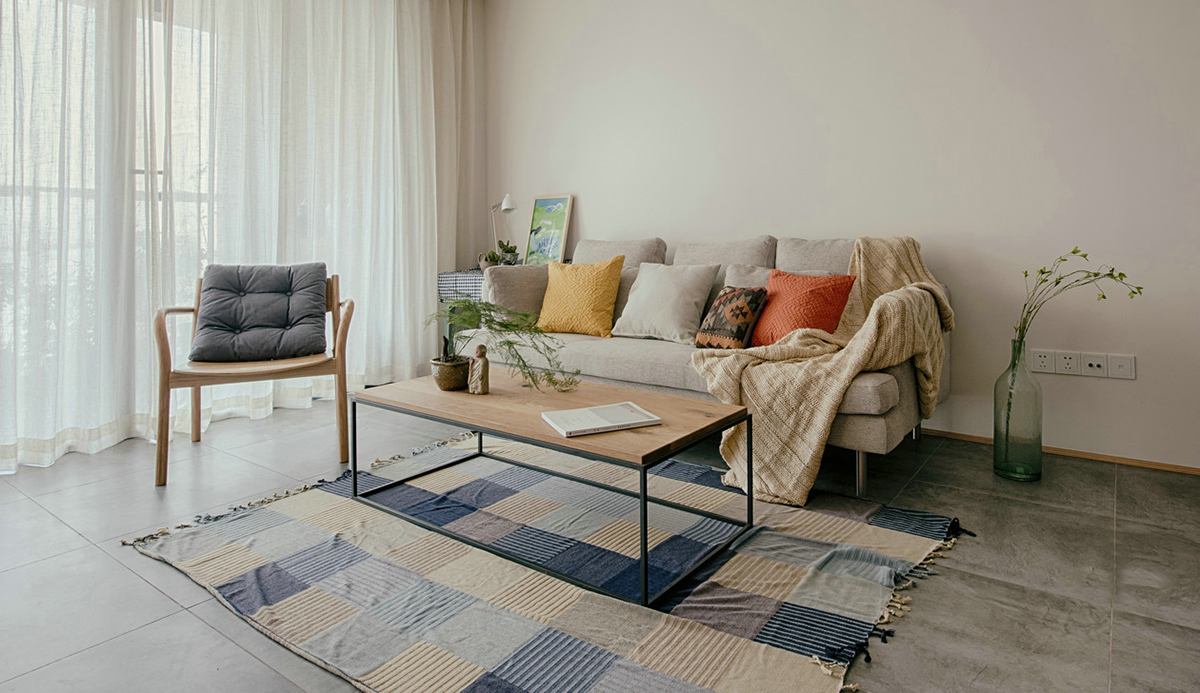 客廳空間開闊明亮。利用淺色紗幔窗簾優化自然光的吸采，讓空間擁有足夠的恬靜感。業主對日式風格很喜歡，客廳的茶幾是業主在日本旅游時帶回國。灰色的布藝沙發，沉穩大氣，搭配自然紋理的原木茶幾和座椅，讓濃郁的日式風情填滿整個空間。柔軟舒適的沙發，隨意擺放著幾個抱枕，再增加一張橙色的真皮單人椅，無形之中提升了空間的質感。
