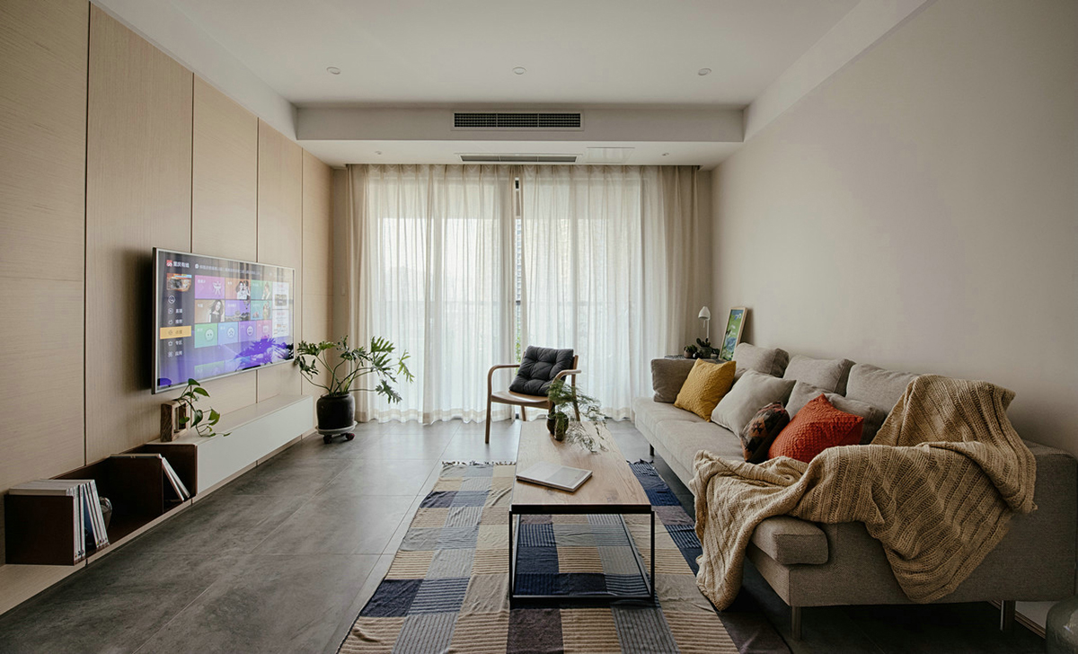 客廳空間開闊明亮。利用淺色紗幔窗簾優化自然光的吸采，讓空間擁有足夠的恬靜感。業主對日式風格很喜歡，客廳的茶幾是業主在日本旅游時帶回國?；疑牟妓嚿嘲l，沉穩大氣，搭配自然紋理的原木茶幾和座椅，讓濃郁的日式風情填滿整個空間。柔軟舒適的沙發，隨意擺放著幾個抱枕，再增加一張橙色的真皮單人椅，無形之中提升了空間的質感。
