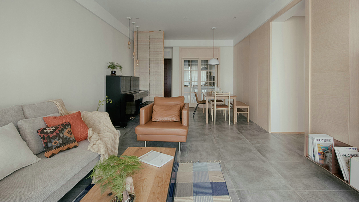 客廳空間開闊明亮。利用淺色紗幔窗簾優化自然光的吸采，讓空間擁有足夠的恬靜感。業主對日式風格很喜歡，客廳的茶幾是業主在日本旅游時帶回國。灰色的布藝沙發，沉穩大氣，搭配自然紋理的原木茶幾和座椅，讓濃郁的日式風情填滿整個空間。柔軟舒適的沙發，隨意擺放著幾個抱枕，再增加一張橙色的真皮單人椅，無形之中提升了空間的質感。
