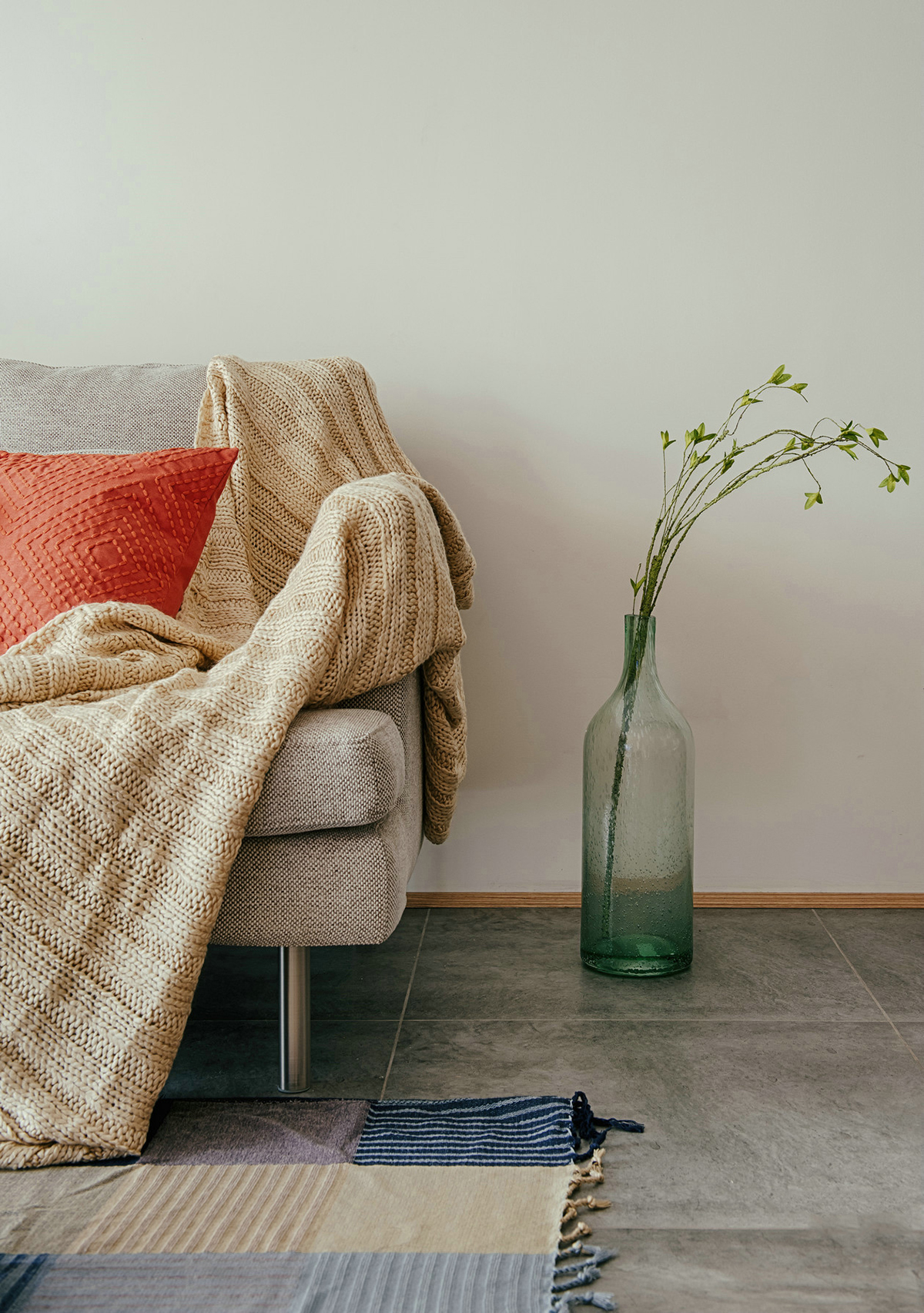 客廳空間開闊明亮。利用淺色紗幔窗簾優化自然光的吸采，讓空間擁有足夠的恬靜感。業主對日式風格很喜歡，客廳的茶幾是業主在日本旅游時帶回國。灰色的布藝沙發，沉穩大氣，搭配自然紋理的原木茶幾和座椅，讓濃郁的日式風情填滿整個空間。柔軟舒適的沙發，隨意擺放著幾個抱枕，再增加一張橙色的真皮單人椅，無形之中提升了空間的質感。
