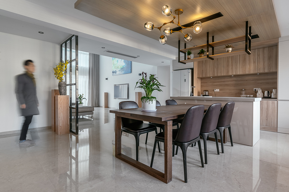 木飾面是貫穿整個(gè)空間的，顏色層次是黑白灰+木色的基調(diào)。大面積白色會(huì)使空間沒有很冷，所以用木色的溫潤(rùn)來(lái)調(diào)節(jié)整個(gè)空間溫度。讓家的感覺更溫馨。櫥柜與頂面不是一家生產(chǎn)，在施工中先確定了櫥柜顏色。帶著樣板去定制頂面顏色，整體效果基本一致。櫥柜和吧臺(tái)的位置就是原來(lái)的空中花園，打通后空間開闊，可以和客廳統(tǒng)一。為了配合整體簡(jiǎn)潔干凈的感覺，窗簾我選用木色百葉窗。透光和隱私性和布藝窗簾同等。右側(cè)的廚房是紅橡制作，為了保證實(shí)木的本質(zhì)只做了清漆。顏色質(zhì)感是市場(chǎng)銷售產(chǎn)品所達(dá)不到的。
